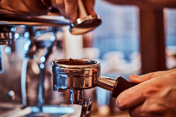 Fototapeta na wymiar Close-up photo of a barista hand holding a portafilter with a black ground coffee in a cafe shop or restaurant