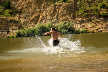 A young man runs, dives into a wide river.  Outdoor activities