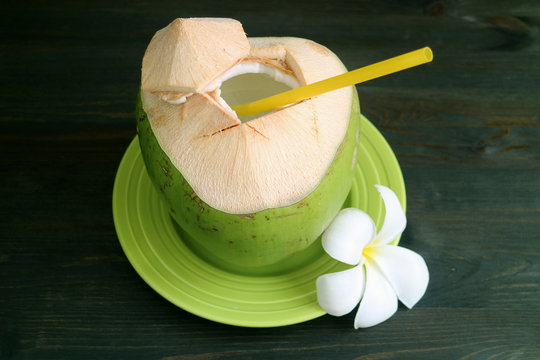 Fresh young coconut with yellow straw and Plumeria flower served on green plate ready for drinking