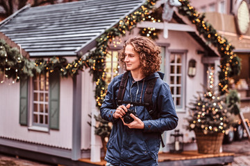 A young handsome curly traveler smiles, walks through the holiday city and takes pictures
