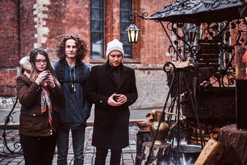 Two guys and a girl choose souvenirs, drink hot coffee, pose and smile at the camera walking through the city square