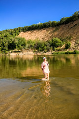 A young woman walks along the broad river, a blue sky and a steep hill of sand