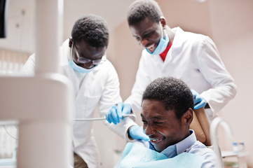 Obraz premium African american man patient in dental chair. Dentist office and doctor practice concept. Laughter at the workplace. Drilling patient's teeth in clinic.