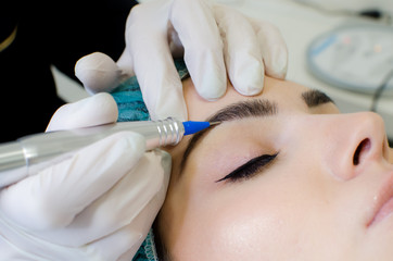 Permanent make-up tattoo, beautician making permanent make up on eyebrows, tattoo procedure on young woman in beauty salon