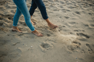 A young couple is having fun and walking on the sea coastline. Legs close up. Romantic date on the beach.