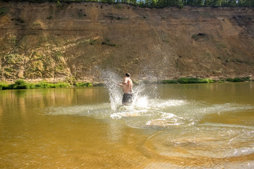 A young man runs, dives into a wide river.  Leisure