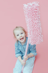 A small child in denim clothes sits on a pink background and holds a pink MOP.