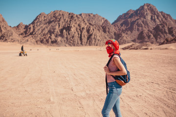 Tourist woman with backpack wearing scarf on head. Traveler admiring Sinai Desert and mountains