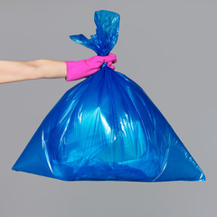 A woman's hand in a rubber glove holds a blue plastic bag full of garbage.