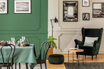 Open plan living and dining room interior with table with chairs and emerald green armchair