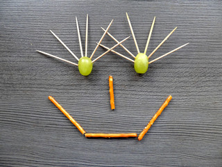 Funny face made of food (grapes and salty sticks). Smiley expression