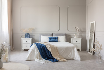 King size bed with grey, blue and white bedding between two wooden nightstands with flowers in...