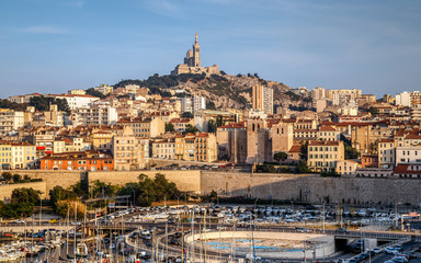 Fototapeta premium Panoramic cityscape of Marseille with the church Notre-Dame de la Garde, landmark of the city, on a hilltop at sunset. Marseille, Provence, France. Holidays in France.