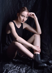 Obraz na płótnie Canvas Sitting beautiful woman in black top and shoes in dark studio.