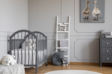 Plush toy on pouf in front of grey bed in child's bedroom interior with ladder and poster. Real...