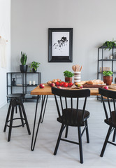 Real photo of a dining table with food, black chairs and painting on a wall in a dining room interior
