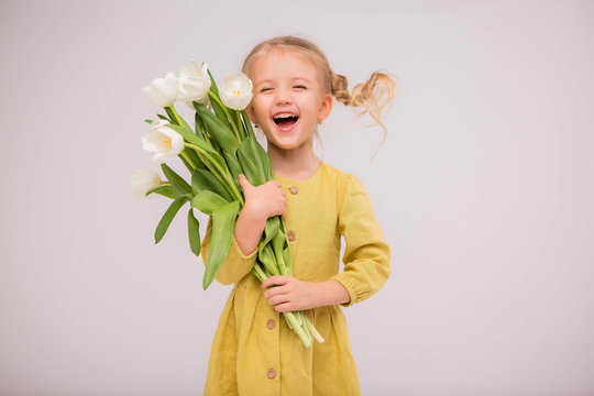 baby girl blonde with a bouquet of tulips on a light background.baby girl blonde smiling.spring and women's day concept.Cute little girl holding white tulips.copy spase