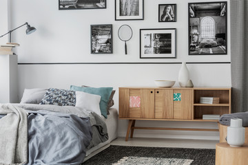 Unique wooden cabinet next to comfortable bed with pillows and grey duvet