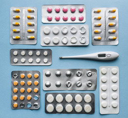 Yellow, white, pink tablets in blisters and thermometer on a blue background top view. Medical pharmacy concept. Traditional medicine.