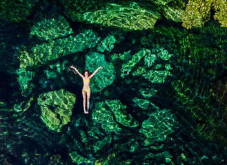 Overhead shot of a attractive young brunette woman in a bikini floating in the Cristalino cenote near Tulum, Mexico. - obrazy, fototapety, plakaty