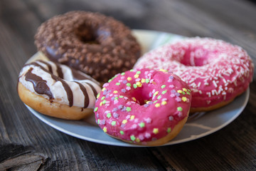 Various donuts on old wooden table. With chocolate fill and nuts, pink glazed and with stars. 