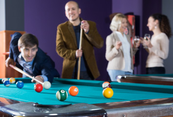 Group of friends playing billiards and smiling in billiard room