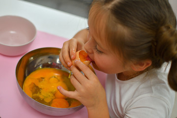 Little girl preparing cookies in kitchen at home. girl tastes raw eggs. Cooking homemade food.Cooking is fun.