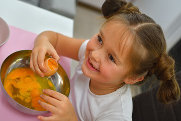 Little girl preparing cookies in kitchen at home. girl tastes raw eggs. Cooking homemade food.Cooking is fun.