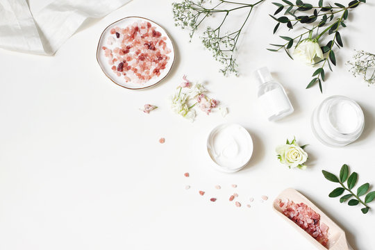 Styled beauty corner, web banner. Skin cream, tonicum bottle, dry flowers, leaves, rose and Himalayan salt. White table background. Organic cosmetics, spa concept. Empty space, flat lay, top view.