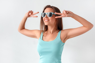 Freestyle. Woman in sunglasses standing studio isolated on white showing peace gesture smiling toothy