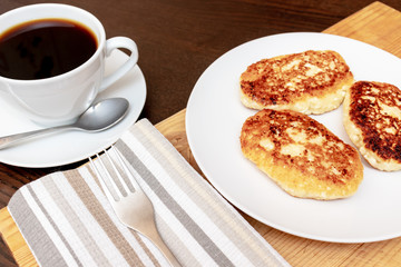 Russian syrniki or sirniki, homemade cottage cheese fritters or pancakes. breakfast with curd pankakes and a cup of coffee