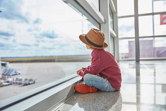Boy sitting behind windowpane at the airport looking at airfield