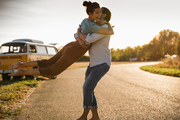 Happy couple doing a road trip with a camper, embracing on the road
