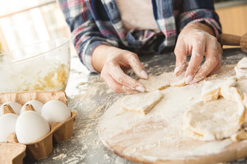 Young housewife at home standing in kitchen cutting out shape from dough close-up