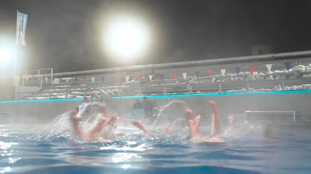 Synchronized swimming. Slender legs girls athletes stick out of the water in open pool in winter. Young girls learn swimming in the pool. Young girls are trained to competitive swimming in the pool