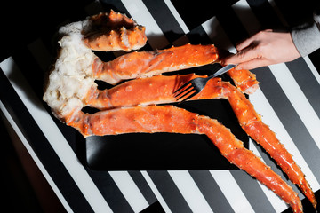 Hand with fork on background of king crabs legs, top view, gourmet seafood