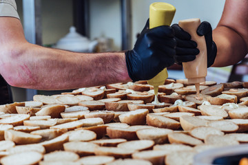 Female and Male Chef Putting Ingredients of Burgers on a Sliced Bread Spread on a Table in Black Gloves - Concept of the Hard Working Person and the Hygiene in the Kitchen