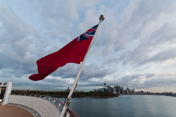 Fototapeta premium View of New York city skyline and upper Hudson river in morning from deck of a cruise ship with red ensign flag in foreground