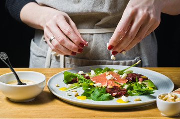 Obraz na płótnie Canvas Chef sprinkles cheese salad with arugula, grapefruit and orange. Black background, side view, kitchen