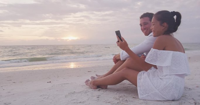 Phone - couple using smartphone app having fun laughing on romantic beach vacation looking at mobile cell phone screen. SLOW MOTION.