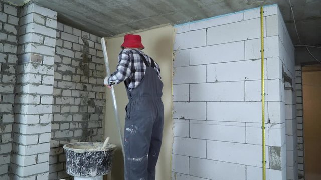 builder leveling plaster on aerated concrete block wall with construction ruler