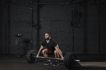 Fototapeta na wymiar Young crossfit athlete doing deadlift exercise with heavy barbell at the gym. Man practicing functional training powerlifting workout