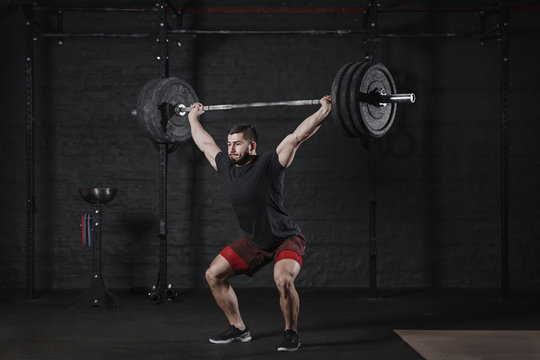 Young crossfit athlete lifting barbell overhead at the gym. Man practicing functional training powerlifting workout exercises