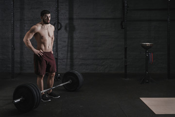 Young cross fit athlete resting after lifting weight at the gym. Handsome man doing functional...