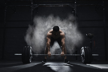 Crossfit athlete preparing to lift heavy barbell in a cloud of dust at the gym. Barbell magnesia protection.