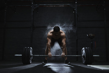 Young crossfit athlete preparing barbell for lifting weight at the gym. Barbell magnesia protection dust cloud. Handsome man doing functional training. Practicing powerlifting. Workout exercises. - Powered by Adobe