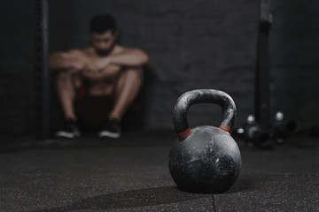 Fototapeta na wymiar Sporty man sitting at the gym suffering breakdown to overcome. Demotivation sport concept. Stress and fatigue in sport. Crossfit kettlebell training.