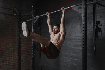 Crossfit athlete doing abs exercises on horizontal bar. Practicing calisthenics at gym. - obrazy, fototapety, plakaty
