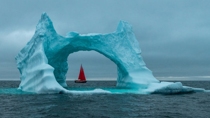 Greenland icerberg arch with red sail ship in Disko bay