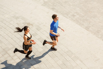 View from above of two young sportsmen wearing tracksuits running together in morning outdoor. Muscular man and fit girl jogging, training and leading healthy lifestyle. Concept of sport.